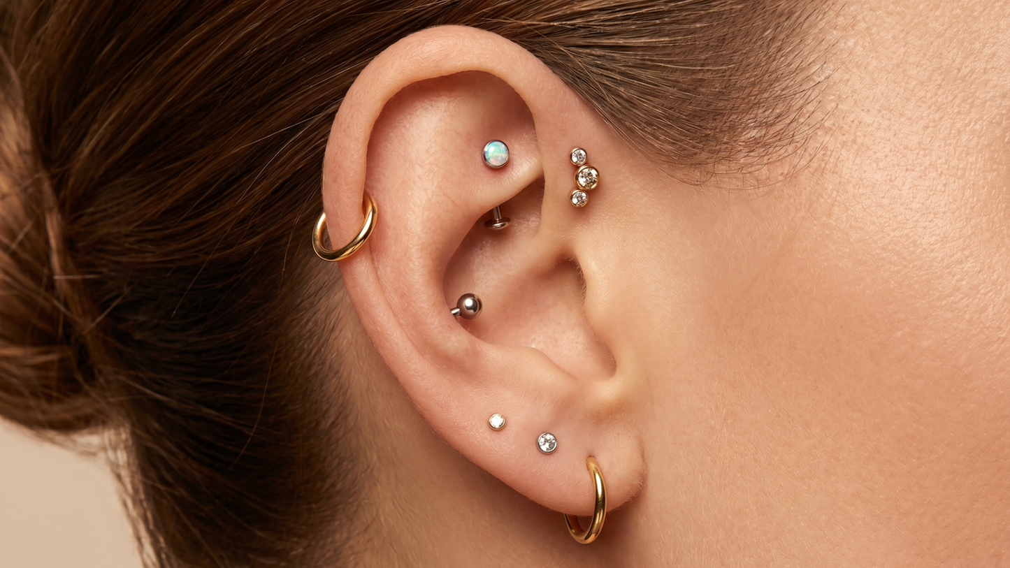 with seven piercings thoughtfully composed: two lobe studs, a small hoop on the third lobe, a flat labret with an opal top, a helix hoop in gold