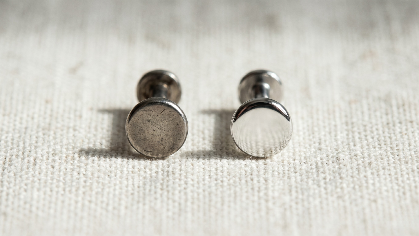 two flat-back labret studs side by side on white linen: on the left, a slightly tarnished steel piece with visible micro-scratches; on the right, a flawless mirror-polished titanium piece
