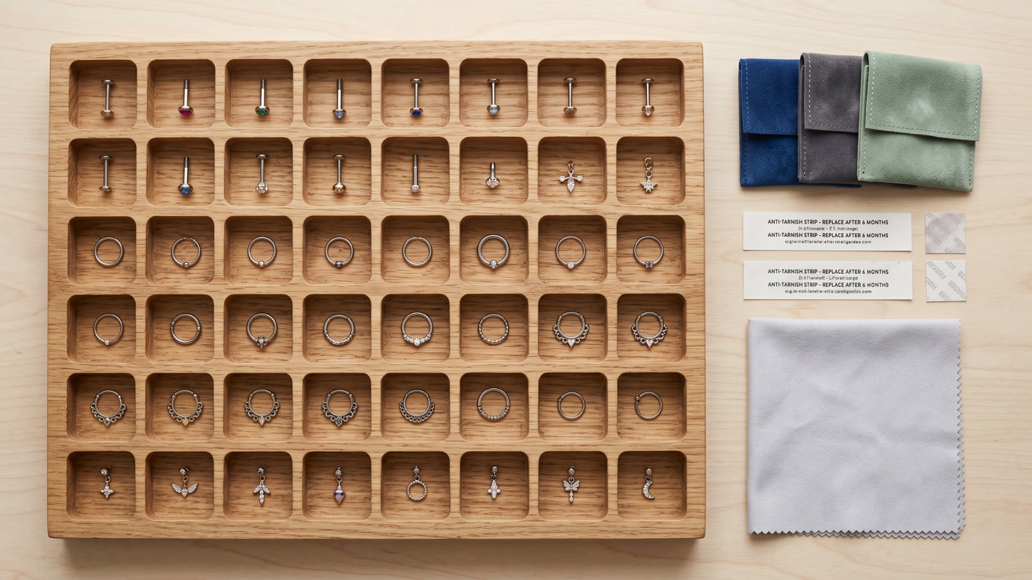 well-organised piercing jewellery storage system: a flat wooden tray with multiple small compartments, each holding a single piece (labrets, hoops, clickers, charms), 