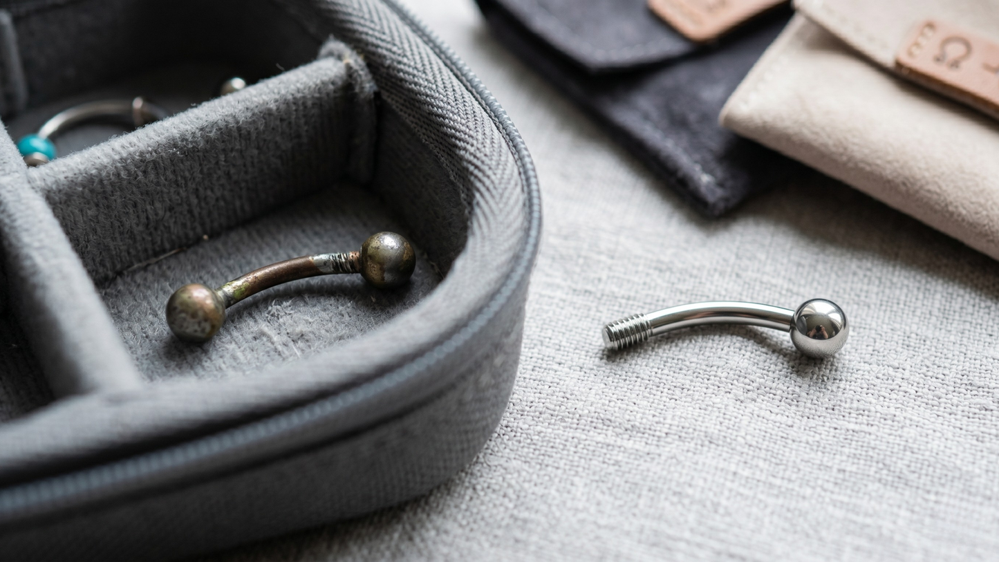 worn piercing jewellery piece with visible coating wear and  damaged threading, sitting alongside a fresh new implant-grade titanium